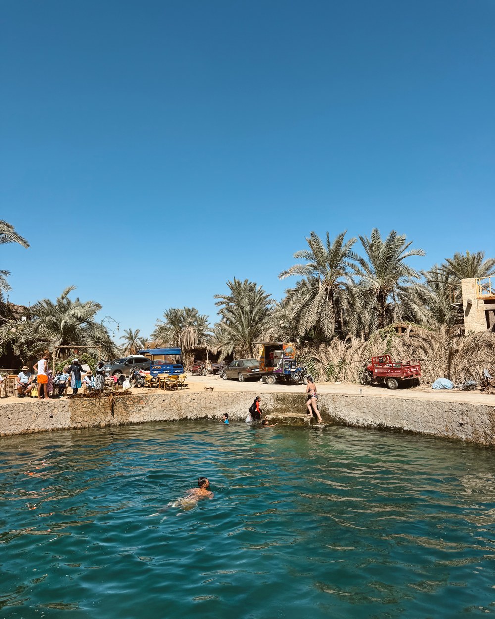 Cleopatra's Spring surrounded by palm trees and cafés in Siwa Oasis