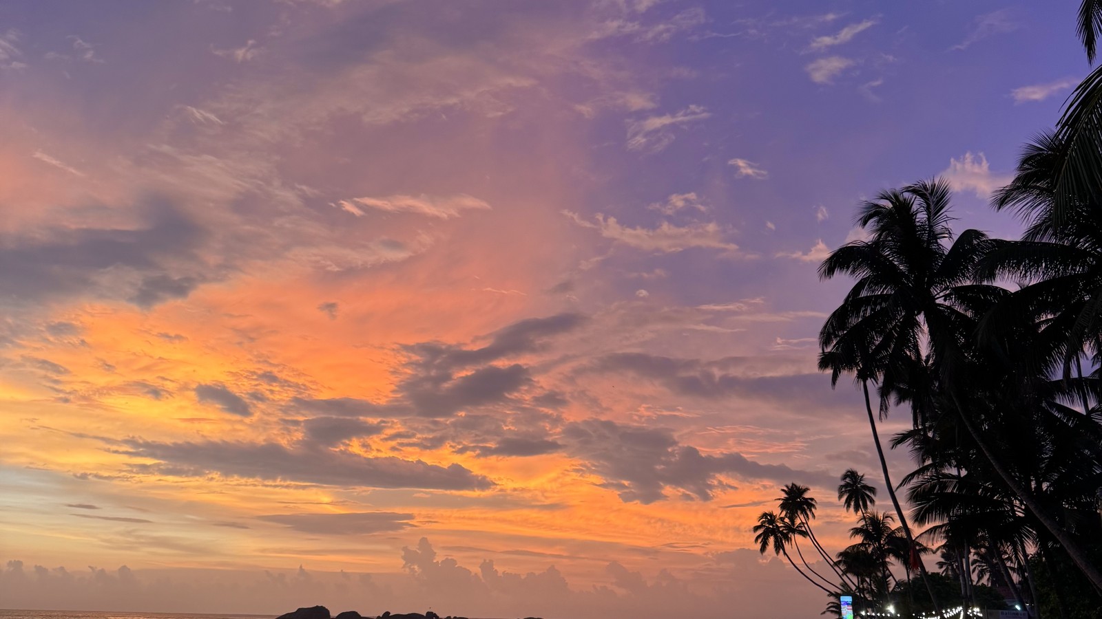 Sunset over the sea with a storm cloud and palm silhouettes on the south coast of Sri Lanka