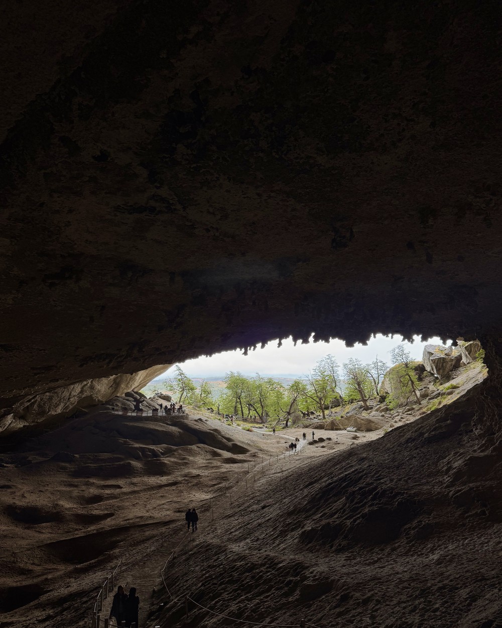 Looking out from inside Cueva del Milodón, with people on the path below the huge rock roof