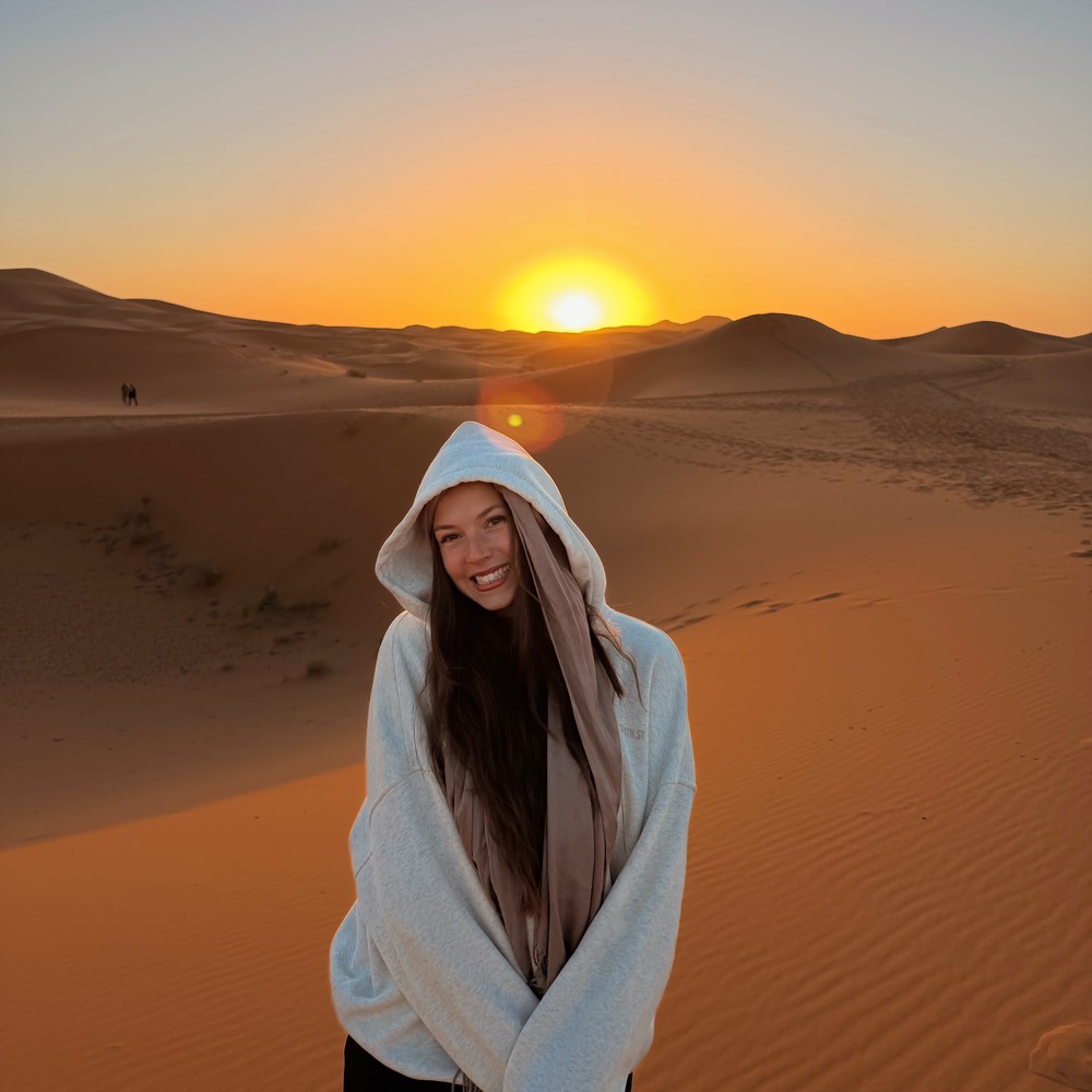 Ellen wrapped in a hoodie in the Sahara Desert, with the low sun above the dunes
