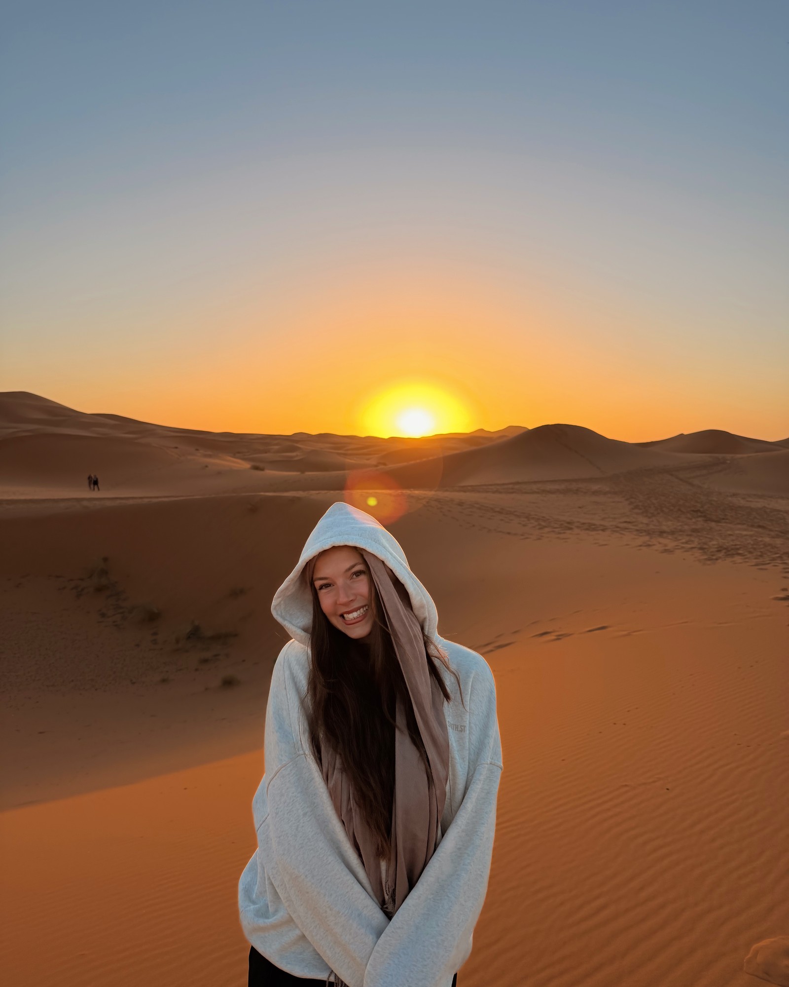 Ellen wrapped in a hoodie in the Sahara Desert, with the low sun above the dunes
