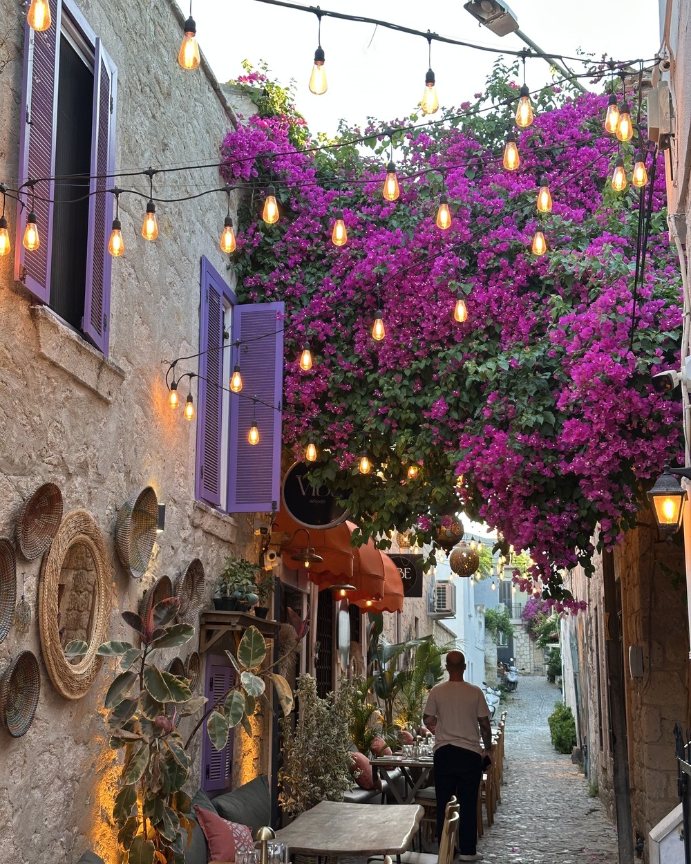 Cobbled street lined with restaurants and bougainvillea in Alaçatı, Türkiye