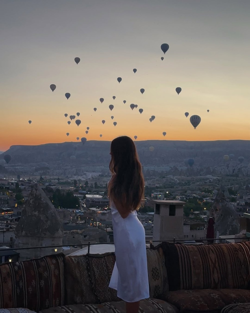 Hot air balloons rising over the valley at sunrise seen from a hotel rooftop in Cappadocia