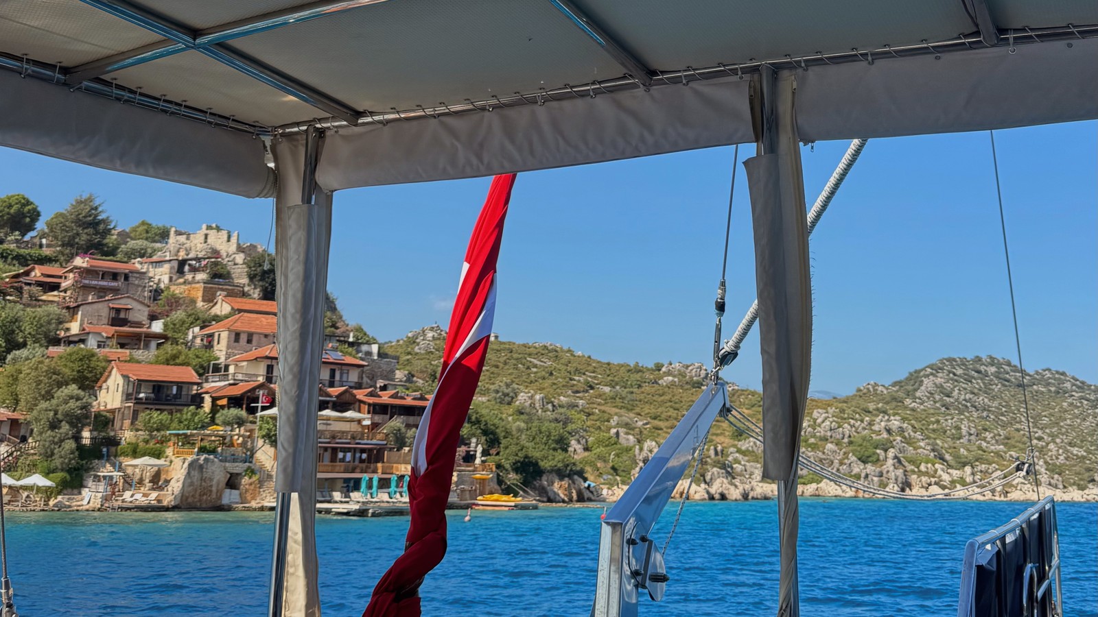 Turkish flag on a gulet deck, with turquoise water and a castle village on the hillside opposite