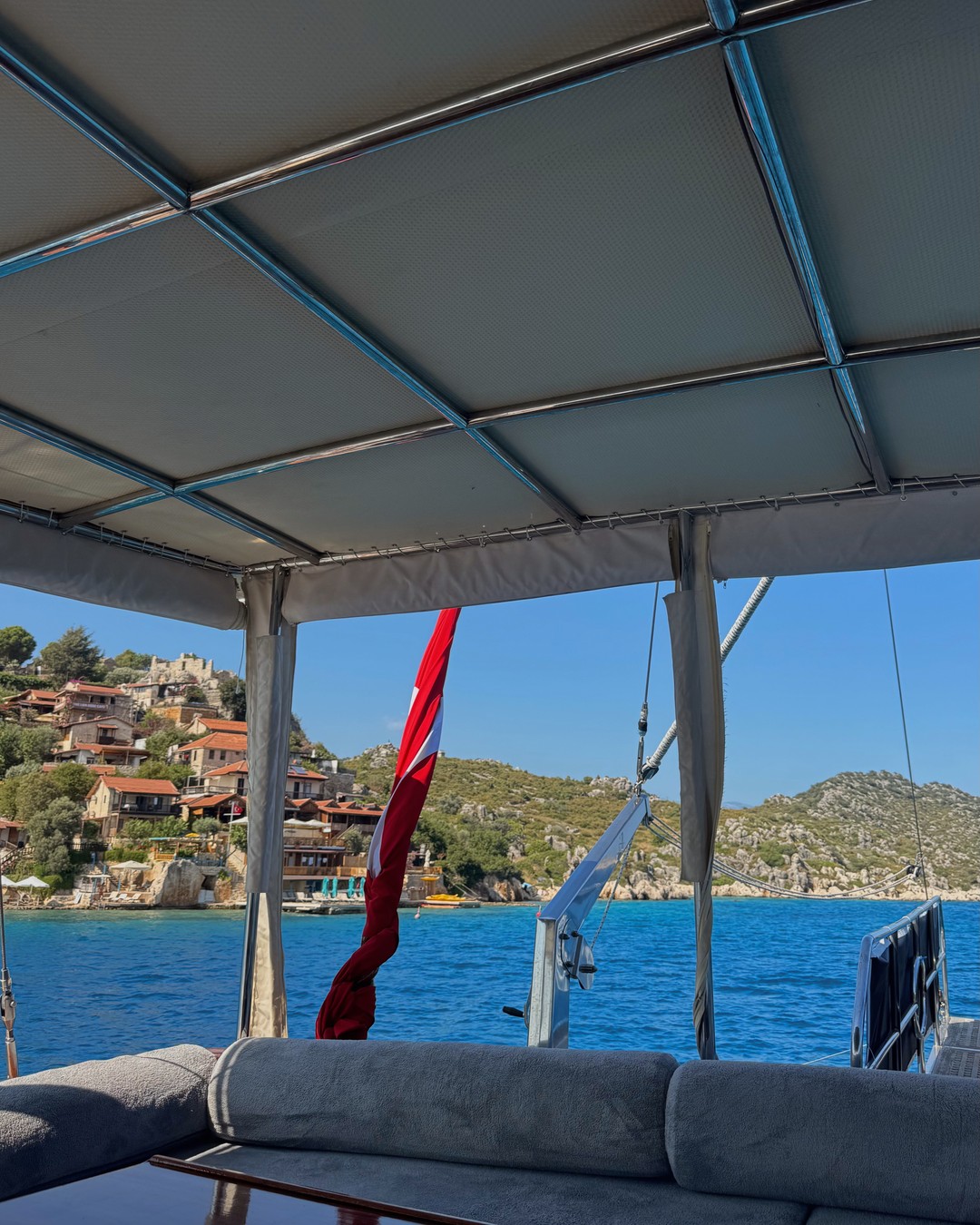 Turkish flag on a gulet deck, with turquoise water and a castle village on the hillside opposite
