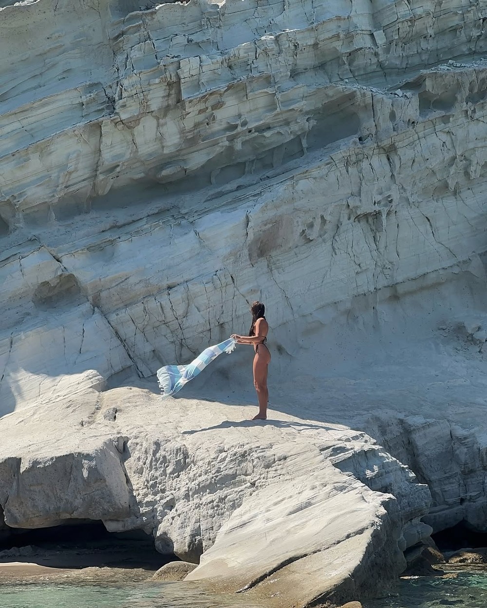 Woman standing on white rock ledges above clear turquoise water at Delikli Koy beach