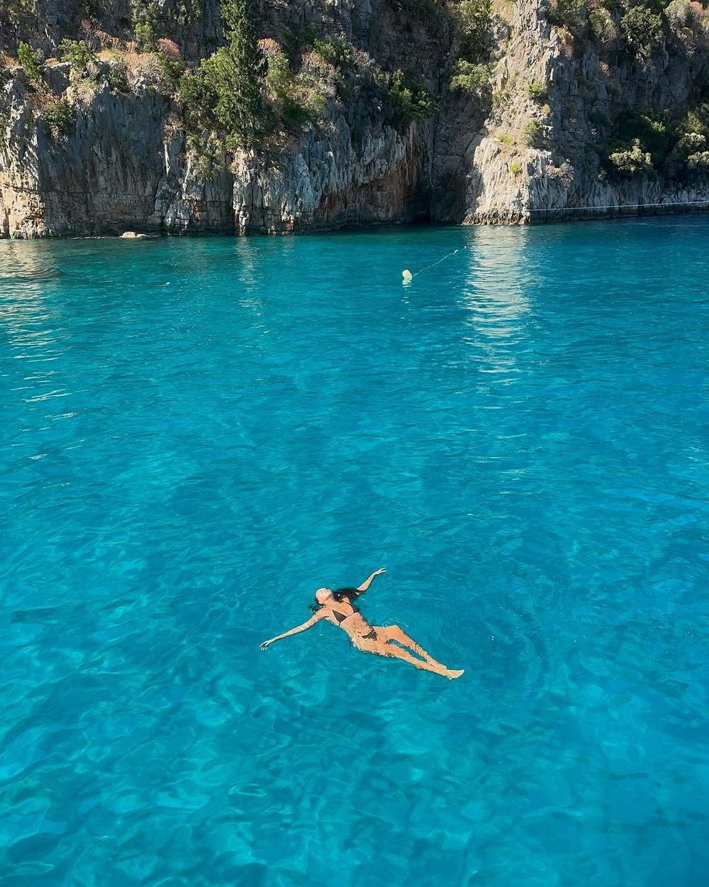 Woman floating in bright turquoise water below white cliffs on the Turkish Riviera