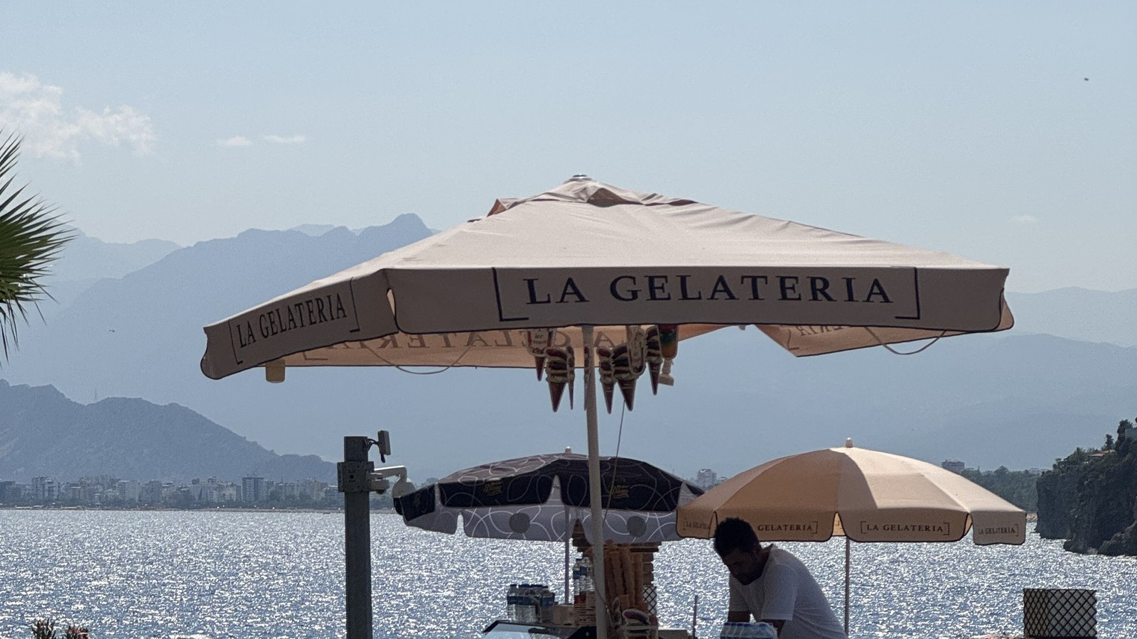 A seafront gelato cart with its vendor under a parasol on the Antalya waterfront