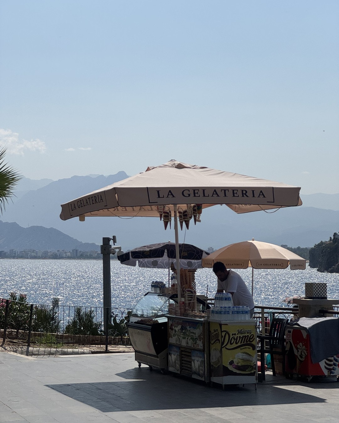 A seafront gelato cart with its vendor under a parasol on the Antalya waterfront