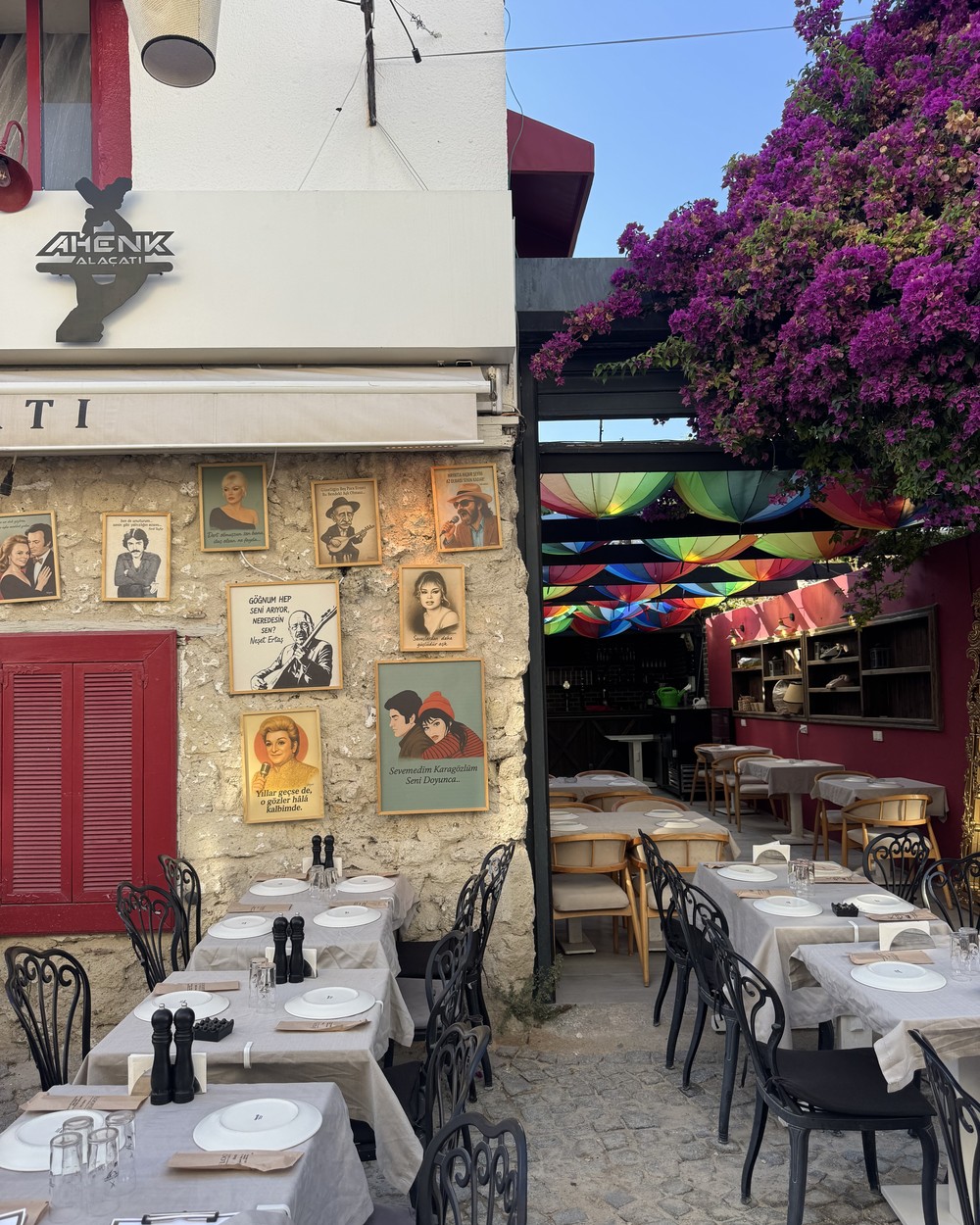 Restaurant terrace with white tablecloths under bougainvillea on a cobbled street in Alaçatı