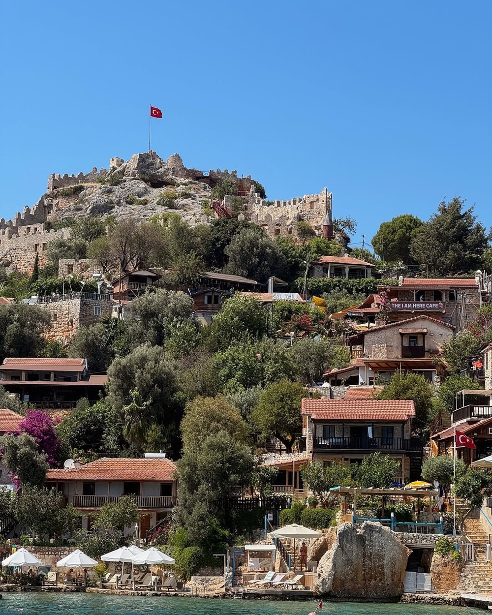Stone village and castle on a green hillside above clear water on the Turkish Riviera