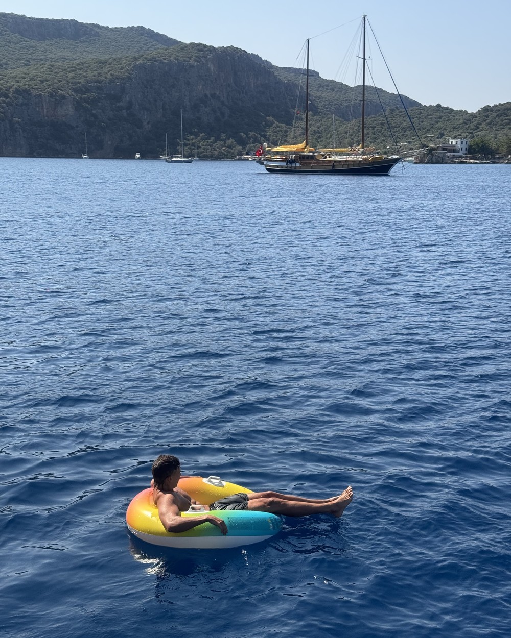 Man floating on an inflatable in deep blue water with a gulet boat behind on the Turkish Riviera