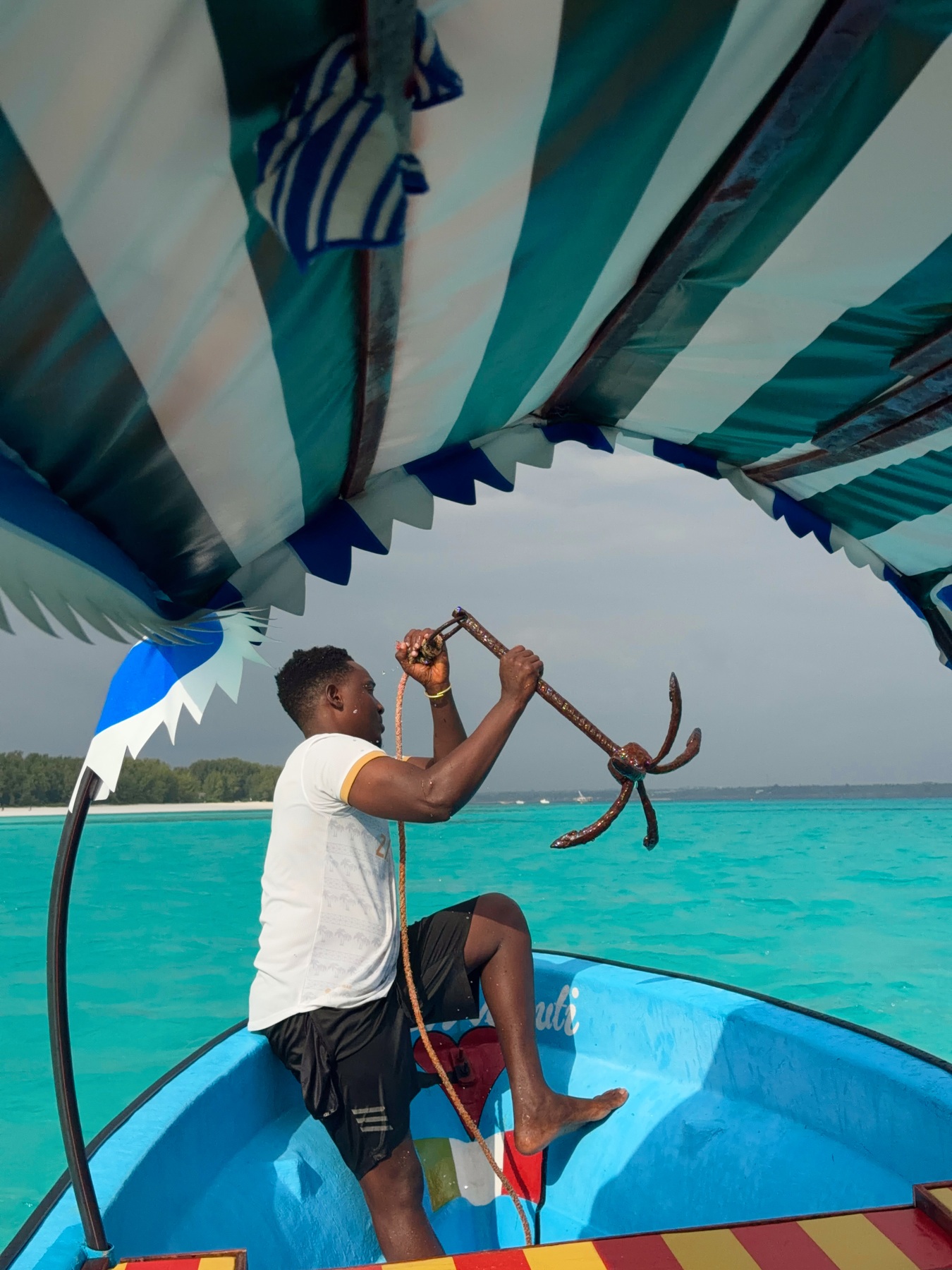 A crew member lifting the anchor aboard our blue boat on turquoise water near Mnemba