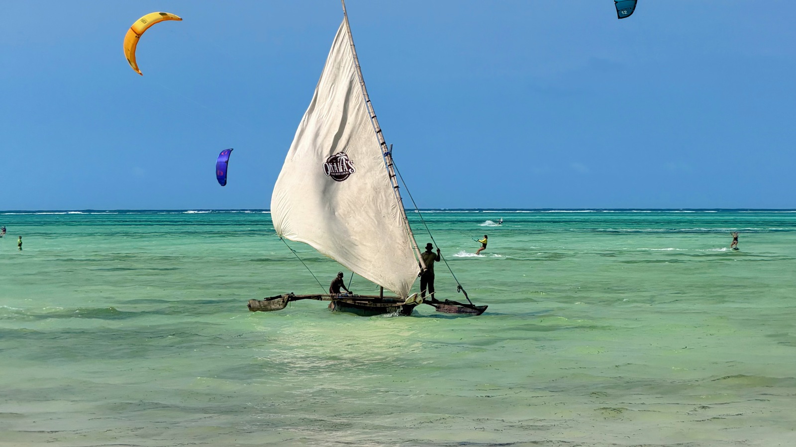 A traditional sailing boat and colourful kites over the turquoise water at Paje beach
