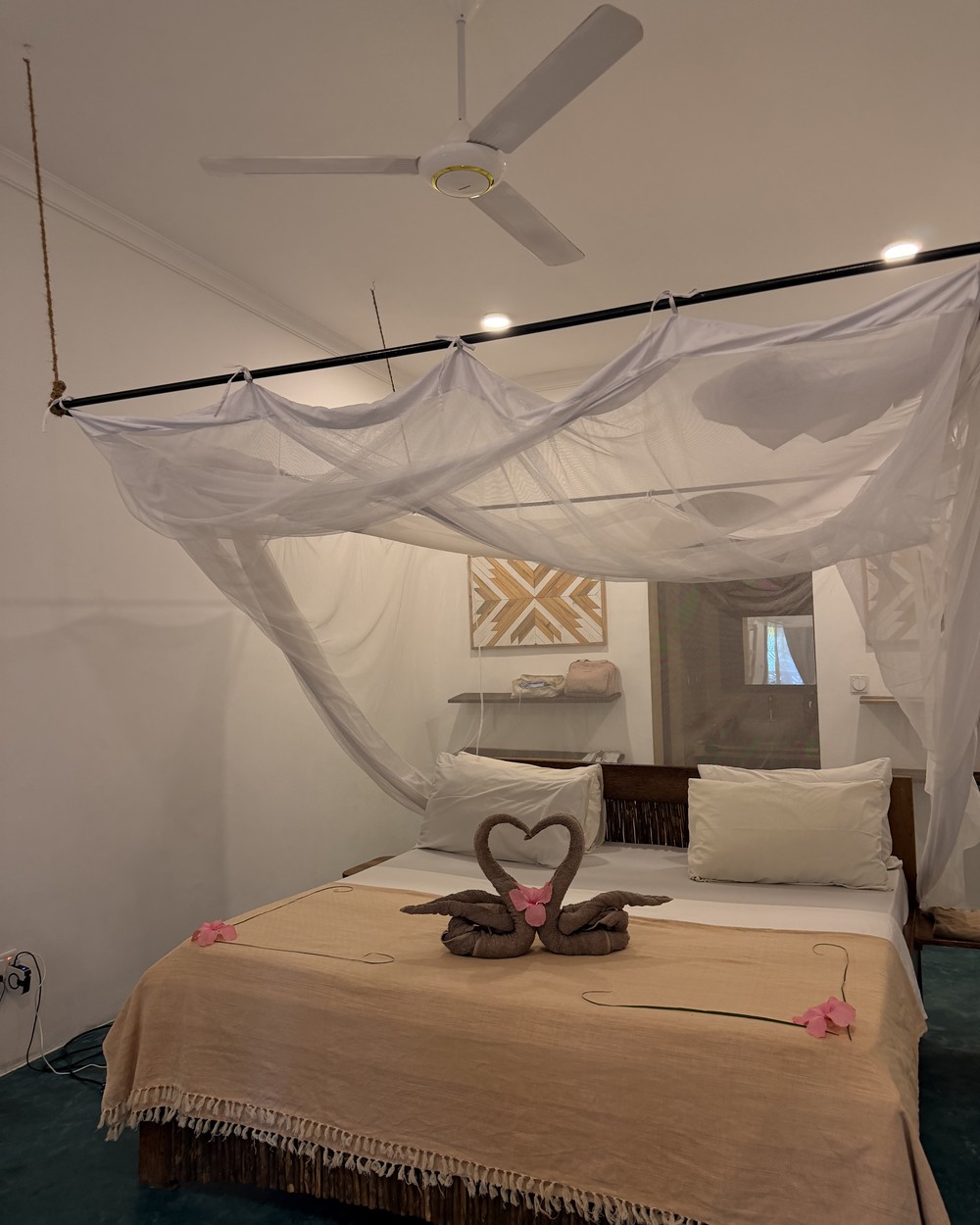 Bed with mosquito netting and swan towel art at Siri Beach Lodge in Nungwi